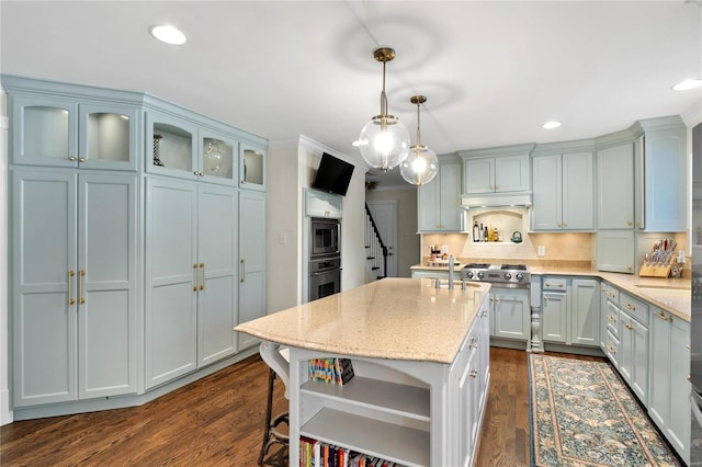 kitchen with dark hardwood / wood-style flooring, decorative backsplash, hanging light fixtures, light stone counters, and a center island with sink