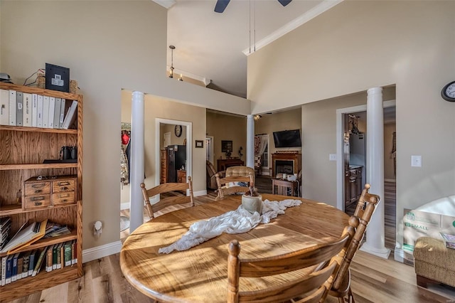 dining space featuring ornate columns, light wood-type flooring, ceiling fan, and a towering ceiling