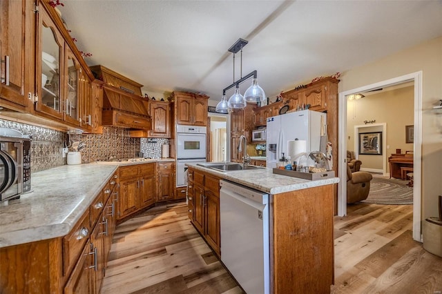 kitchen with sink, tasteful backsplash, decorative light fixtures, a center island with sink, and white appliances