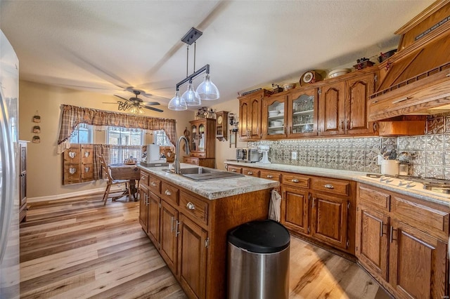 kitchen featuring sink, light wood-type flooring, pendant lighting, a kitchen island with sink, and backsplash