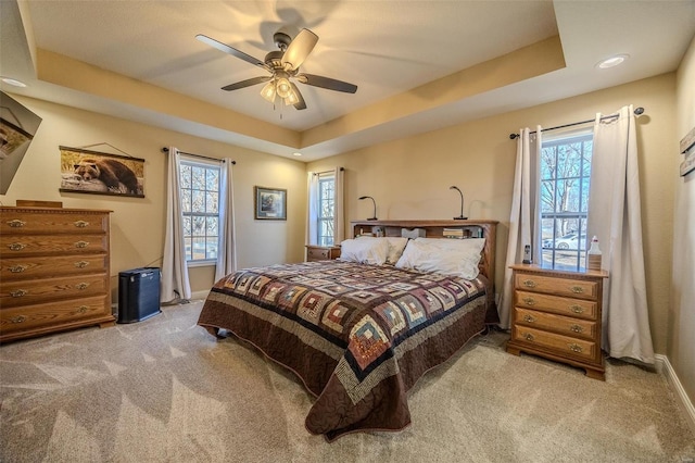 bedroom featuring light carpet, a tray ceiling, and ceiling fan