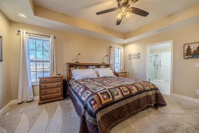 bedroom with a tray ceiling, light colored carpet, ceiling fan, and ensuite bathroom