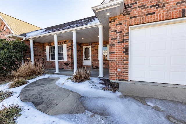 snow covered property entrance featuring a porch and a garage