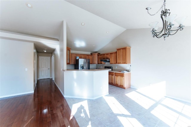 kitchen with pendant lighting, high vaulted ceiling, kitchen peninsula, stainless steel refrigerator with ice dispenser, and an inviting chandelier