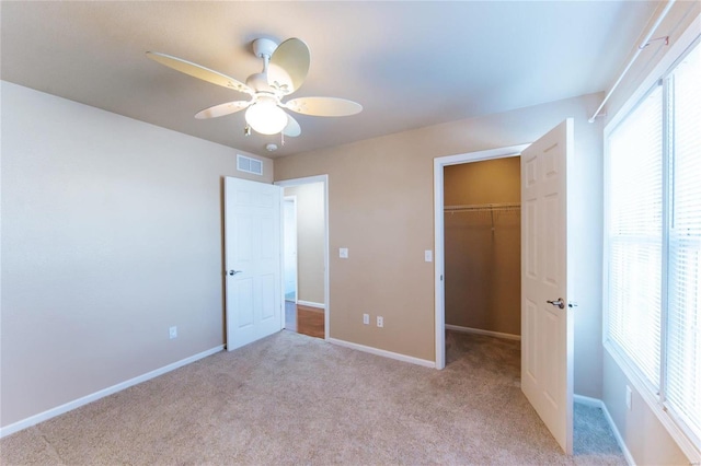 unfurnished bedroom featuring light carpet, a spacious closet, a closet, and ceiling fan