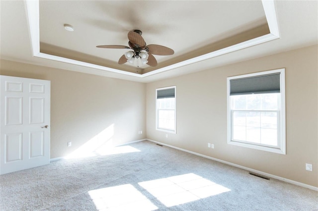 carpeted empty room with ceiling fan and a tray ceiling