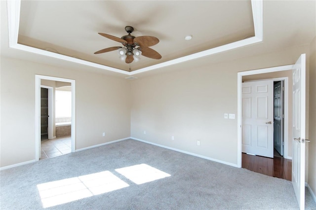 spare room featuring light carpet, ceiling fan, and a tray ceiling