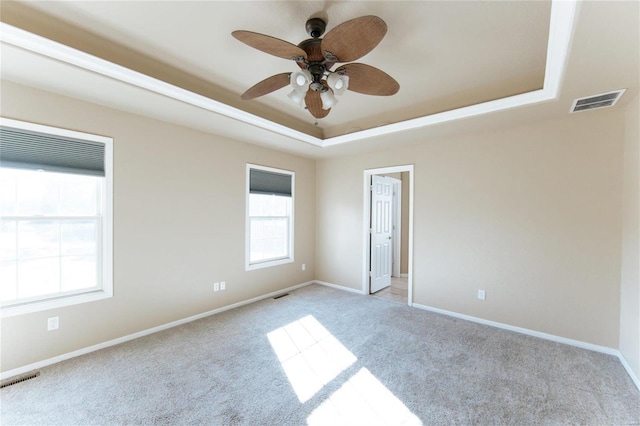 empty room featuring light carpet, a tray ceiling, and ceiling fan