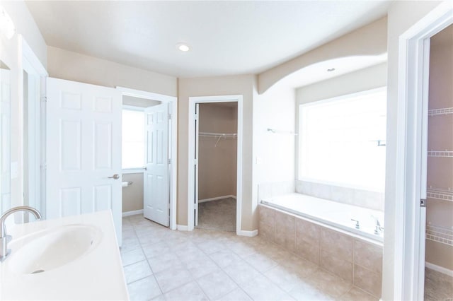 bathroom featuring tiled tub, vanity, and tile patterned flooring