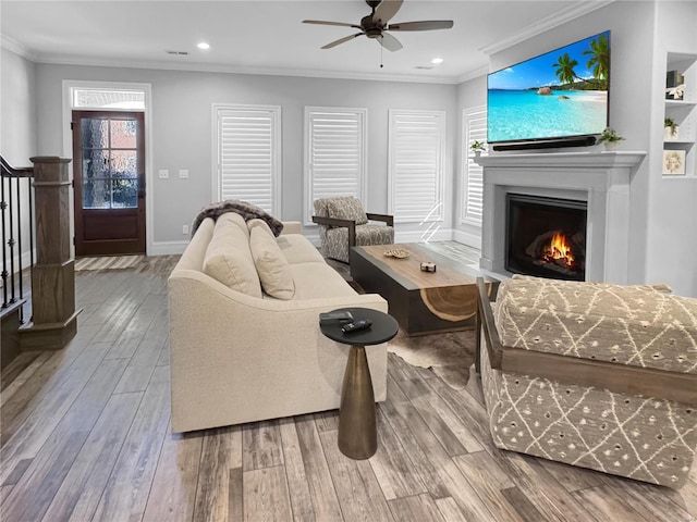 living room featuring ceiling fan, wood-type flooring, built in shelves, and crown molding