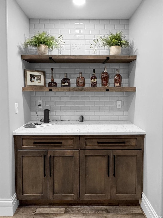 bar with light stone countertops, dark brown cabinets, and tasteful backsplash