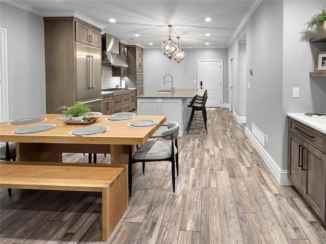 kitchen with pendant lighting, wall chimney range hood, a center island with sink, and crown molding