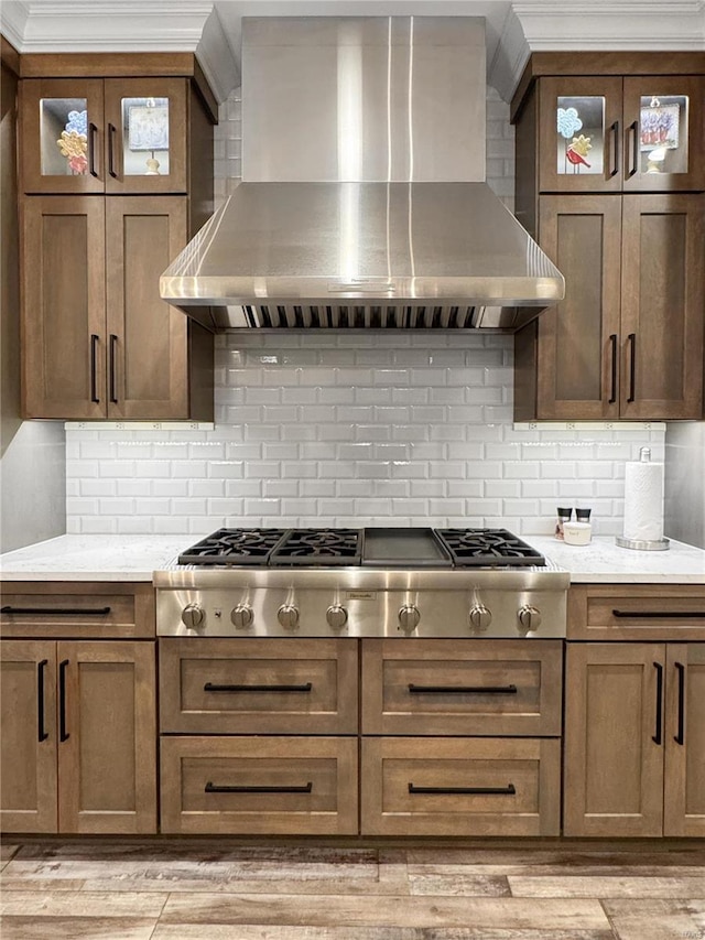 kitchen with wall chimney exhaust hood, light stone counters, backsplash, and stainless steel gas cooktop