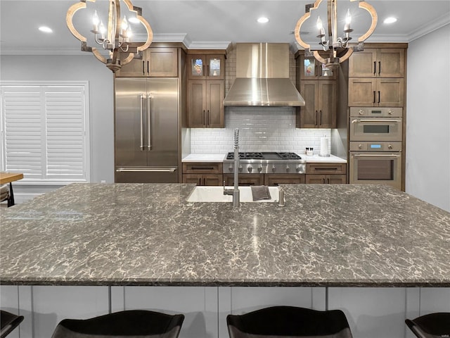 kitchen with a kitchen bar, wall chimney range hood, stainless steel appliances, and an inviting chandelier