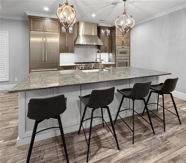 kitchen with a large island, sink, wall chimney range hood, and stainless steel appliances