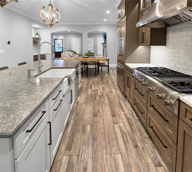 kitchen with extractor fan, decorative light fixtures, white cabinetry, sink, and ornamental molding