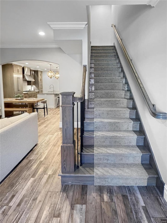 stairway featuring sink, an inviting chandelier, crown molding, and hardwood / wood-style floors