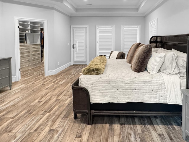 bedroom featuring a walk in closet, hardwood / wood-style flooring, ornamental molding, and a tray ceiling