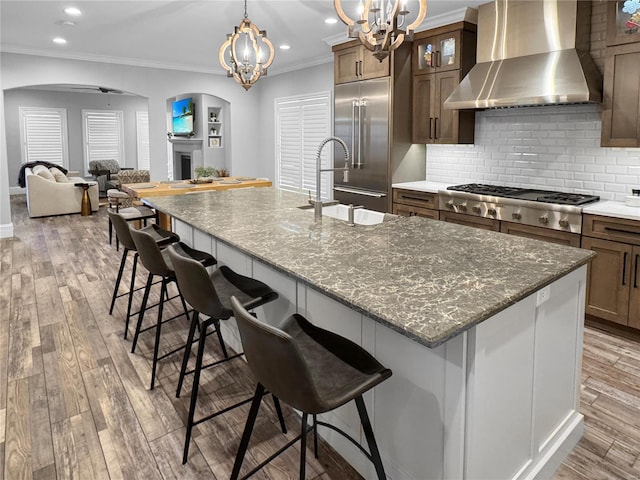 kitchen featuring wall chimney range hood, a breakfast bar, dark stone countertops, stainless steel appliances, and an island with sink