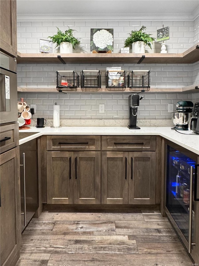 bar with dark brown cabinetry, ornamental molding, hardwood / wood-style flooring, beverage cooler, and backsplash