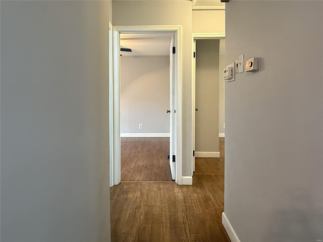 corridor featuring baseboards and dark wood-style flooring