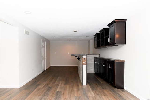 kitchen featuring baseboards, a kitchen bar, visible vents, and dark wood finished floors