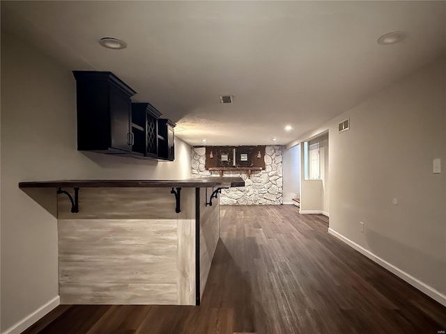 kitchen with dark wood finished floors, a kitchen bar, visible vents, and baseboards