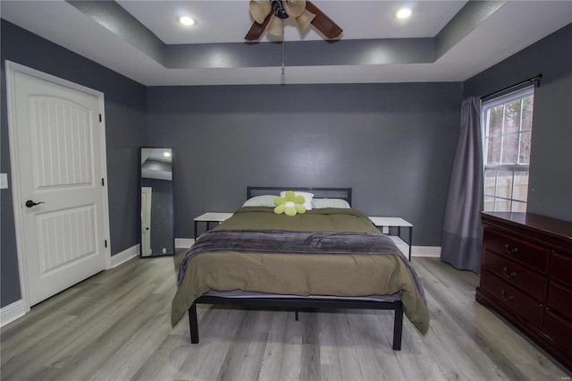 bedroom featuring light wood-type flooring, ceiling fan, and a tray ceiling