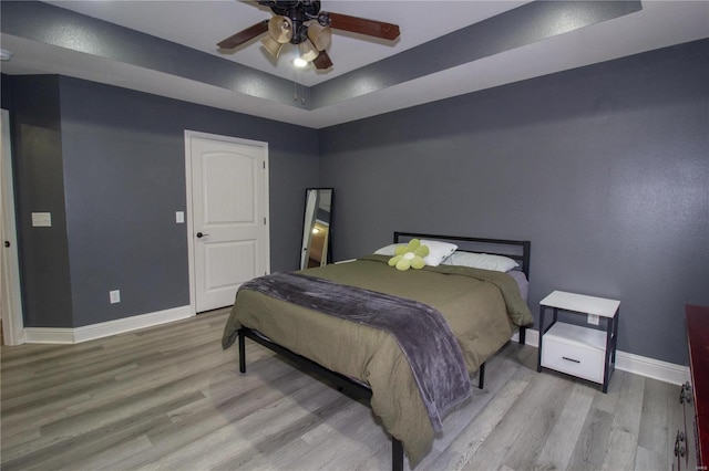 bedroom with ceiling fan, a raised ceiling, and light wood-type flooring