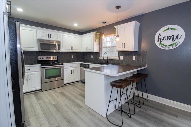 kitchen featuring white cabinets, stainless steel appliances, sink, hanging light fixtures, and kitchen peninsula