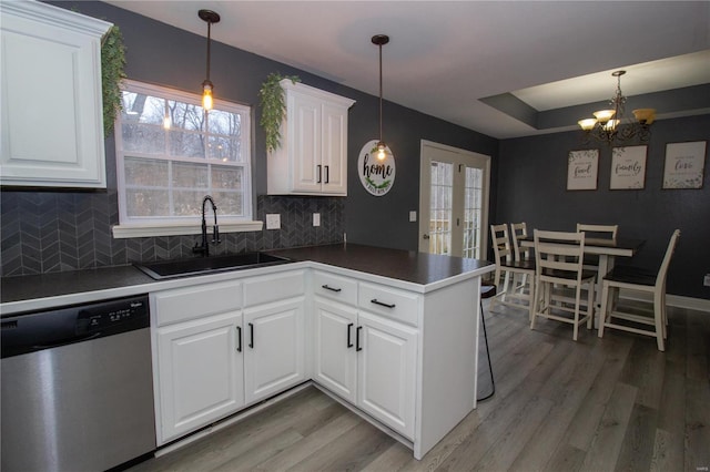 kitchen with kitchen peninsula, stainless steel dishwasher, hanging light fixtures, sink, and white cabinets