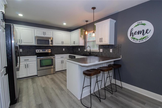 kitchen with pendant lighting, white cabinetry, stainless steel appliances, sink, and kitchen peninsula