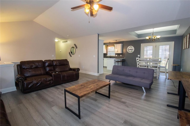 living room featuring vaulted ceiling, sink, hardwood / wood-style flooring, a tray ceiling, and ceiling fan with notable chandelier