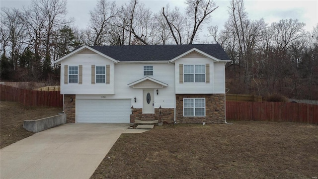 split foyer home featuring stone siding, concrete driveway, an attached garage, and fence