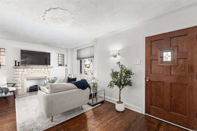 living area featuring a stone fireplace, dark wood-style floors, baseboards, and a textured ceiling