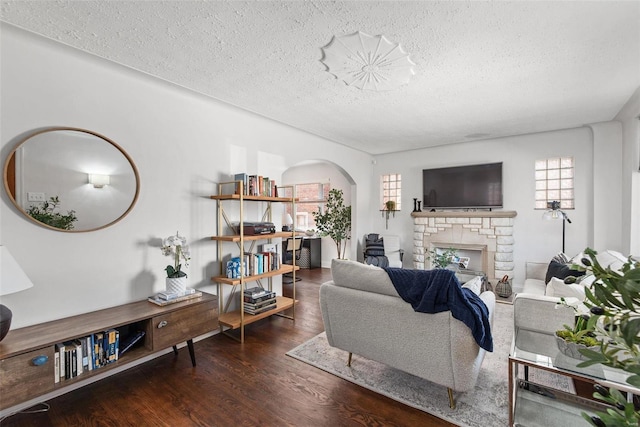 living room featuring arched walkways, a stone fireplace, a textured ceiling, and wood finished floors