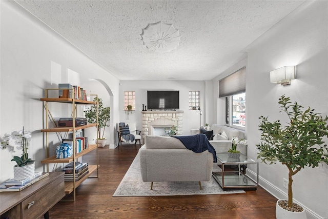 living area featuring wood finished floors, baseboards, arched walkways, a textured ceiling, and a brick fireplace