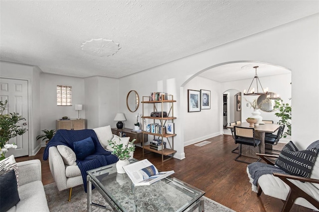 living area featuring visible vents, dark wood-style floors, arched walkways, a notable chandelier, and a textured ceiling