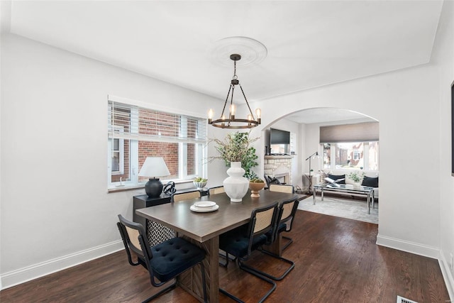 dining area with baseboards, arched walkways, a notable chandelier, and wood finished floors