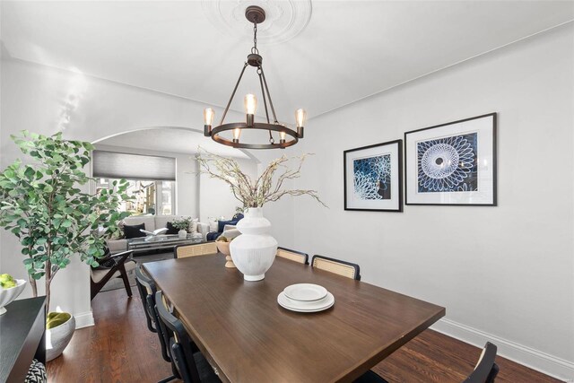 dining area featuring an inviting chandelier, wood finished floors, arched walkways, and baseboards