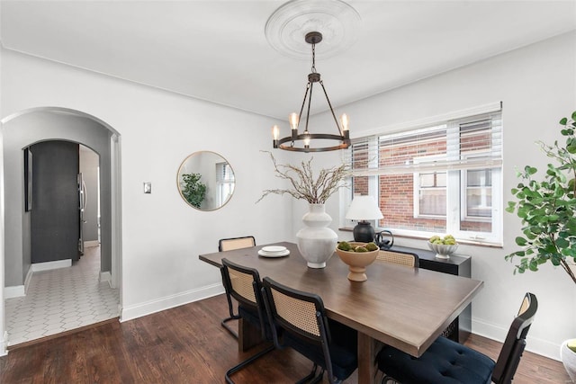 dining space featuring baseboards, arched walkways, wood finished floors, and a chandelier