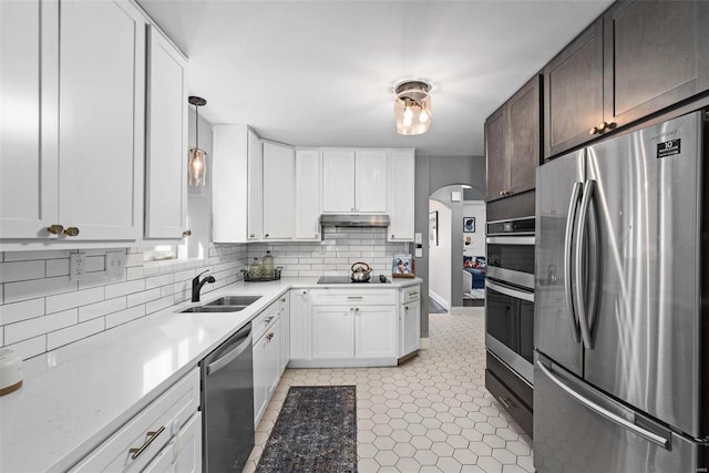 kitchen featuring arched walkways, a sink, stainless steel appliances, under cabinet range hood, and tasteful backsplash