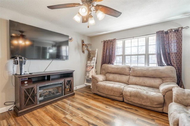 living room with ceiling fan, a textured ceiling, and light wood-type flooring