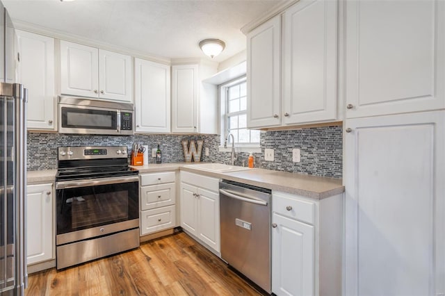 kitchen with white cabinetry, light hardwood / wood-style floors, stainless steel appliances, tasteful backsplash, and sink