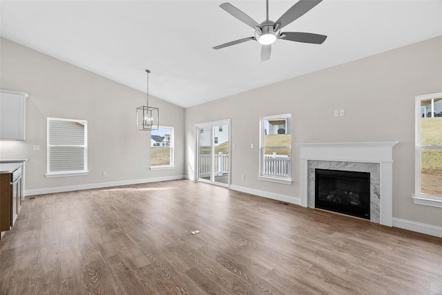 unfurnished living room featuring lofted ceiling, ceiling fan with notable chandelier, a fireplace, and light wood-type flooring