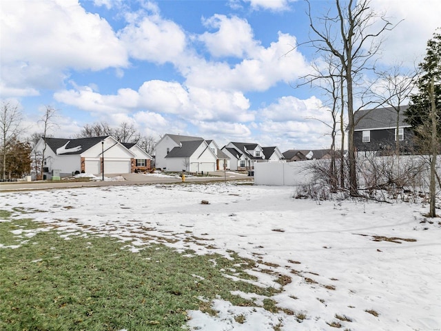 snowy yard featuring a garage, fence, and a residential view