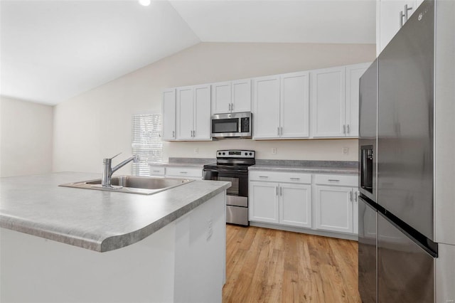 kitchen with stainless steel appliances, lofted ceiling, light wood-style floors, white cabinetry, and a sink