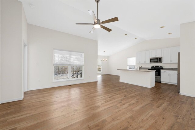 kitchen with light wood finished floors, white cabinets, open floor plan, stainless steel appliances, and ceiling fan with notable chandelier