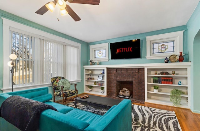 living room with ceiling fan, a brick fireplace, hardwood / wood-style floors, and crown molding