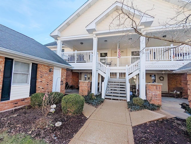 view of front of house with stairway, roof with shingles, a porch, a patio area, and brick siding